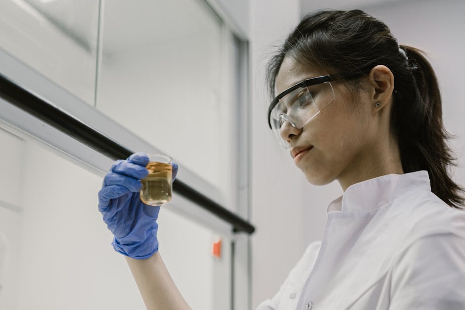 A scientist in protective gear examines a liquid sample in the lab.