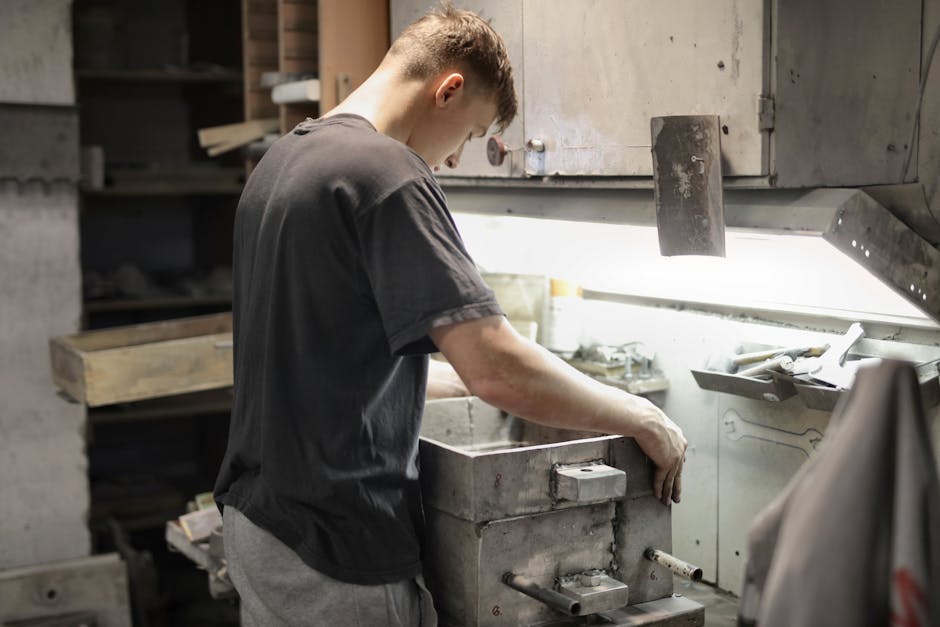 A young male craftsman focuses on metalwork in an industrial workshop.